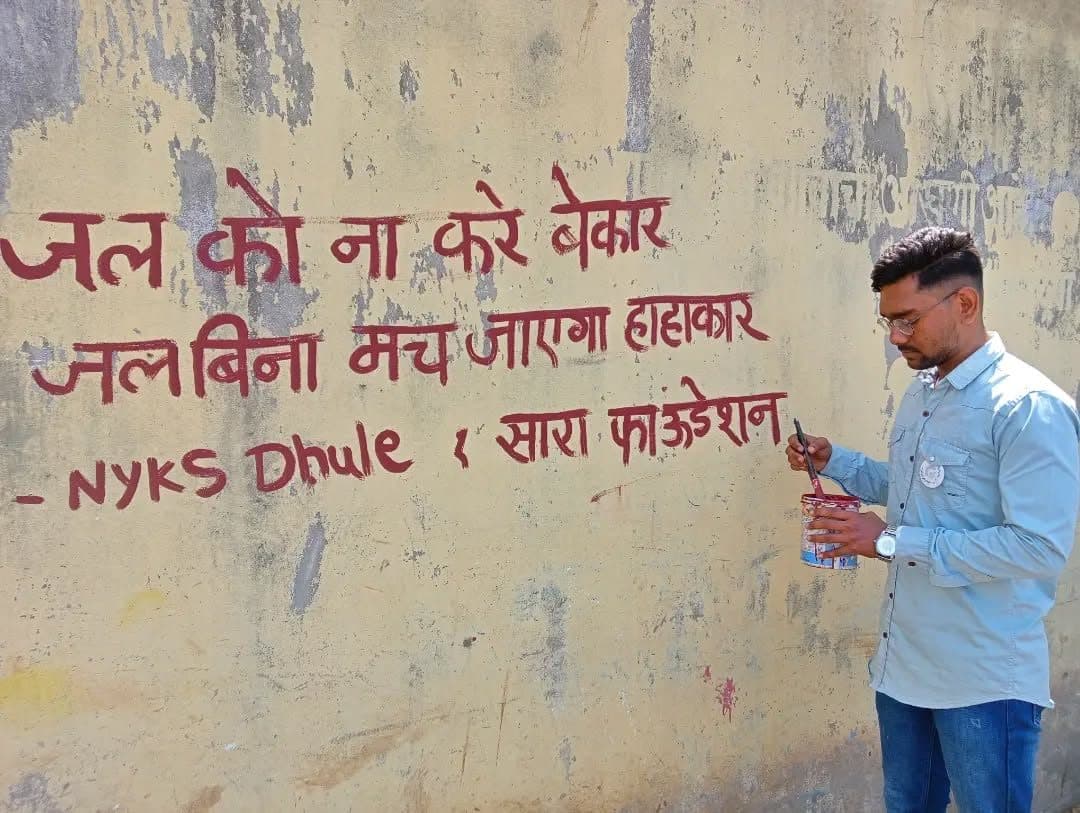 A volunteer painting a water-saving slogan with NYKS Dhule, 2023