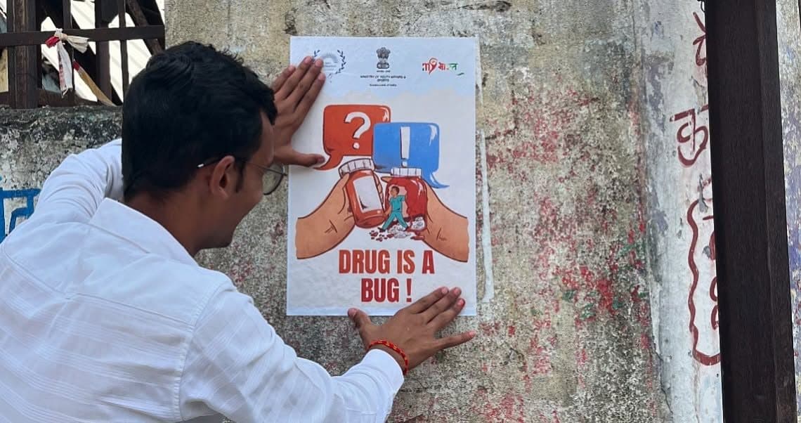 A volunteer putting up a 'Drug is a bug' awareness poster, Dhule, October 2024
